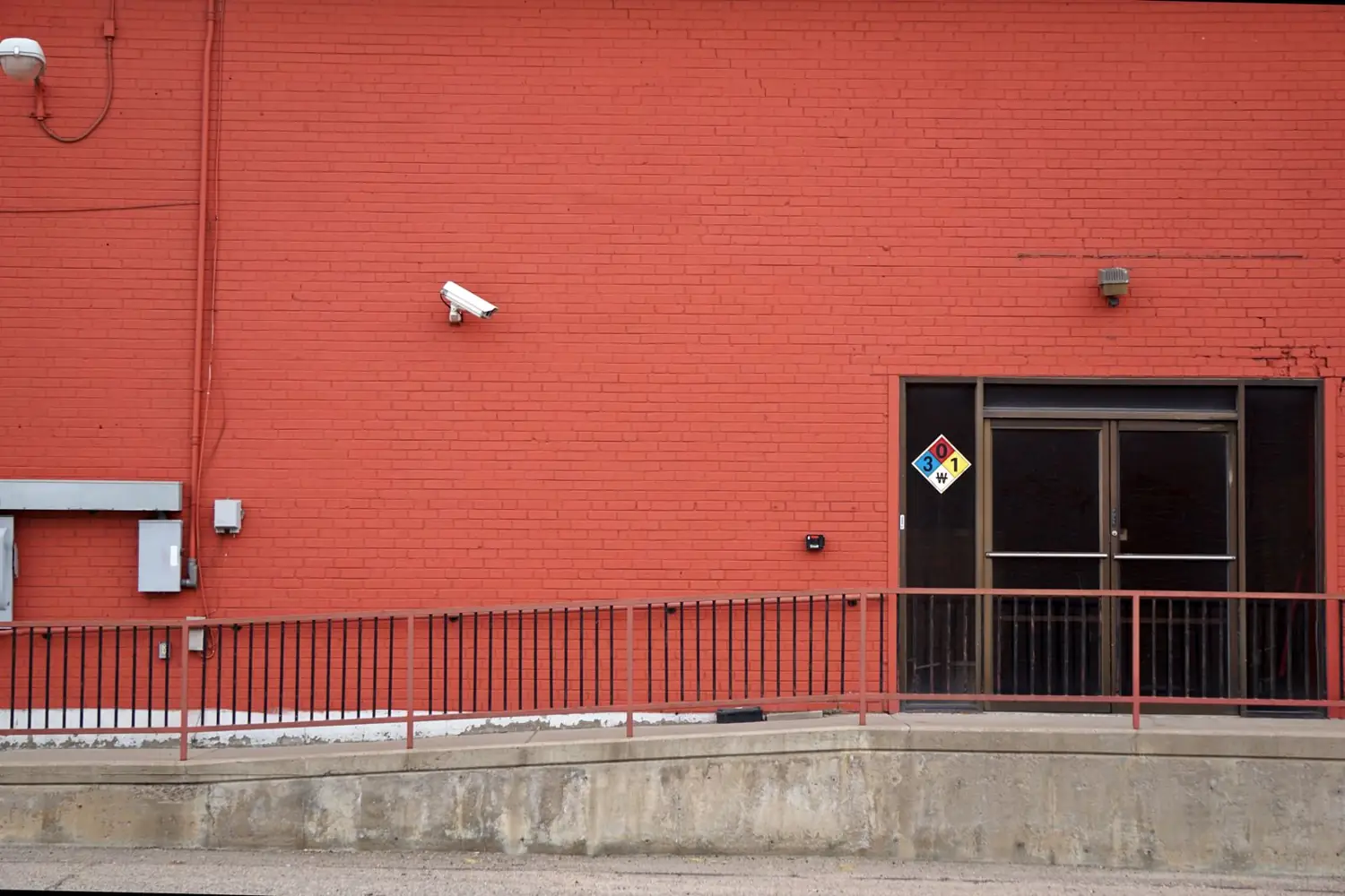 Cámara de vigilancia en un muro rojo junto a señalización de la entrada