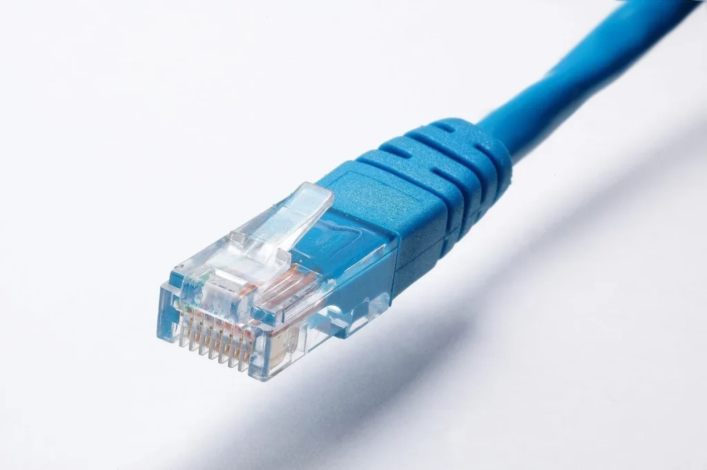 Conector RJ45 transparente con los ocho contactos dorados al final de un cable de red azul