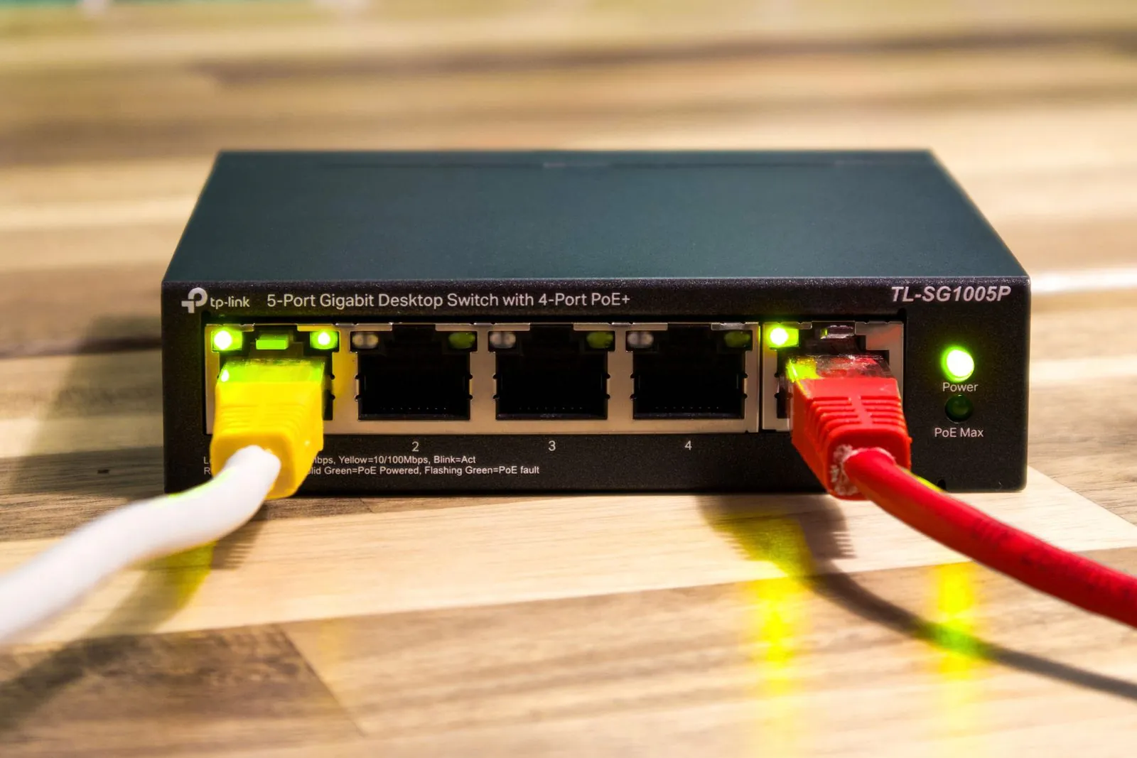 Switch no administrable de cinco puertos con PoE y dos cables de red conectados sobre un escritorio